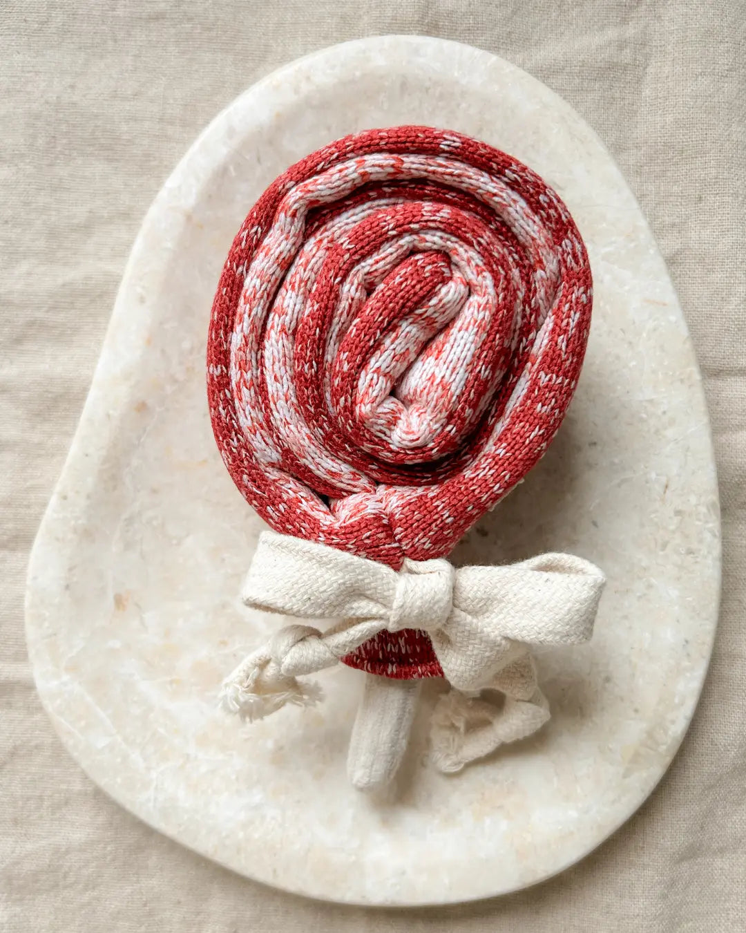 Red and white striped lollipop-shaped dog toy on a marble stone