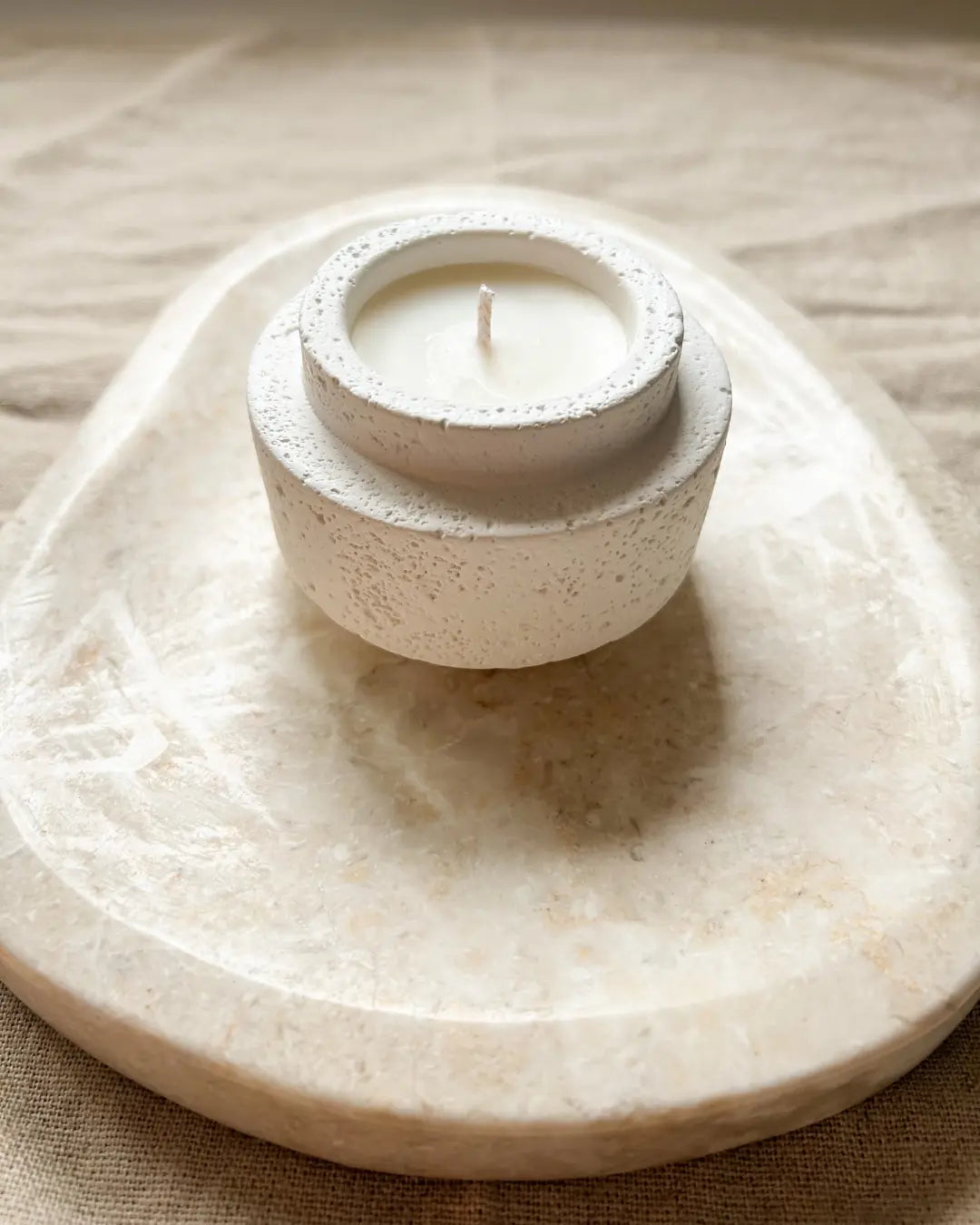 White candle in a textured holder on a marble surface