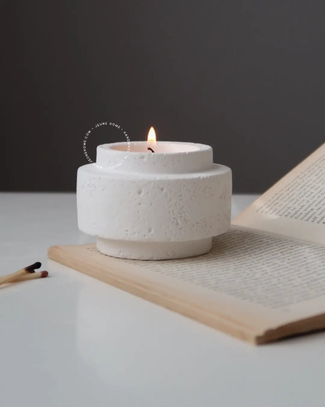 White textured candle holder with a lit candle on an open book against a dark background