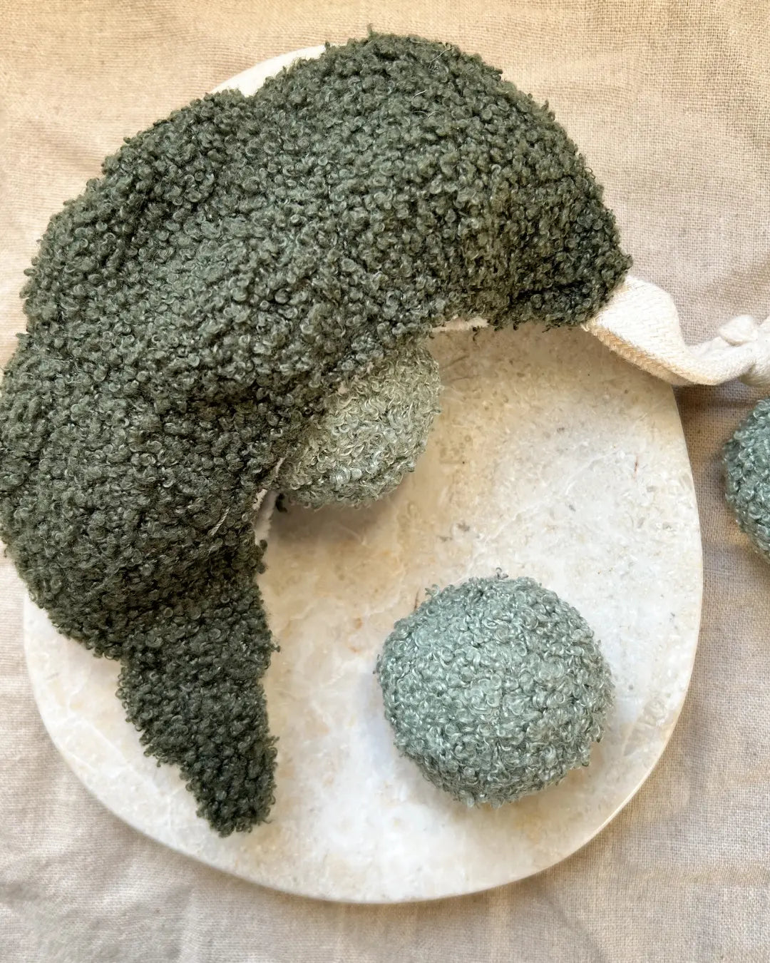Green bouclé pea pod-shaped dog toy with plush green squeaky balls on a neutral marble background