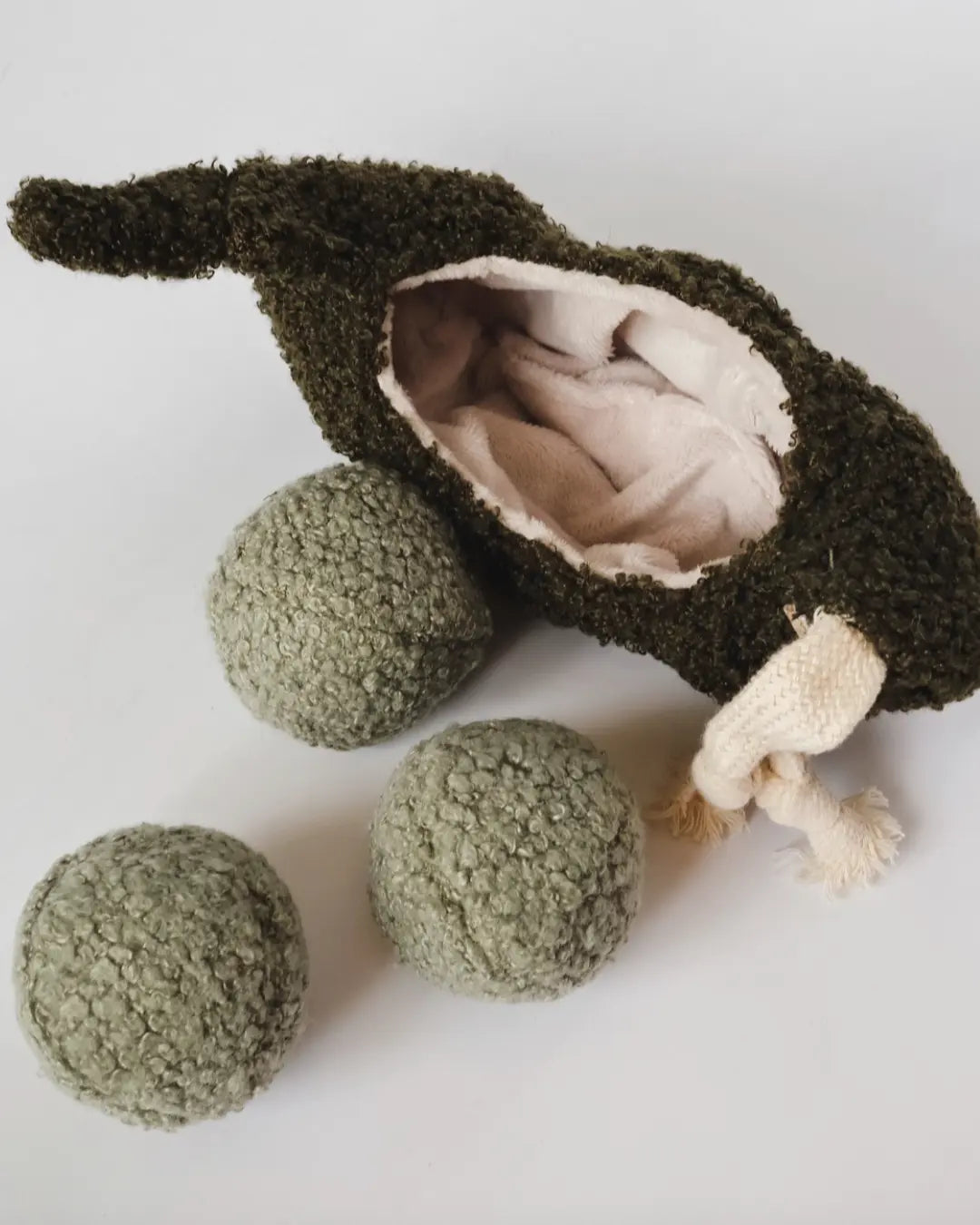 Pea pod-shaped plush dog toy with three inner squeaky balls on a white background