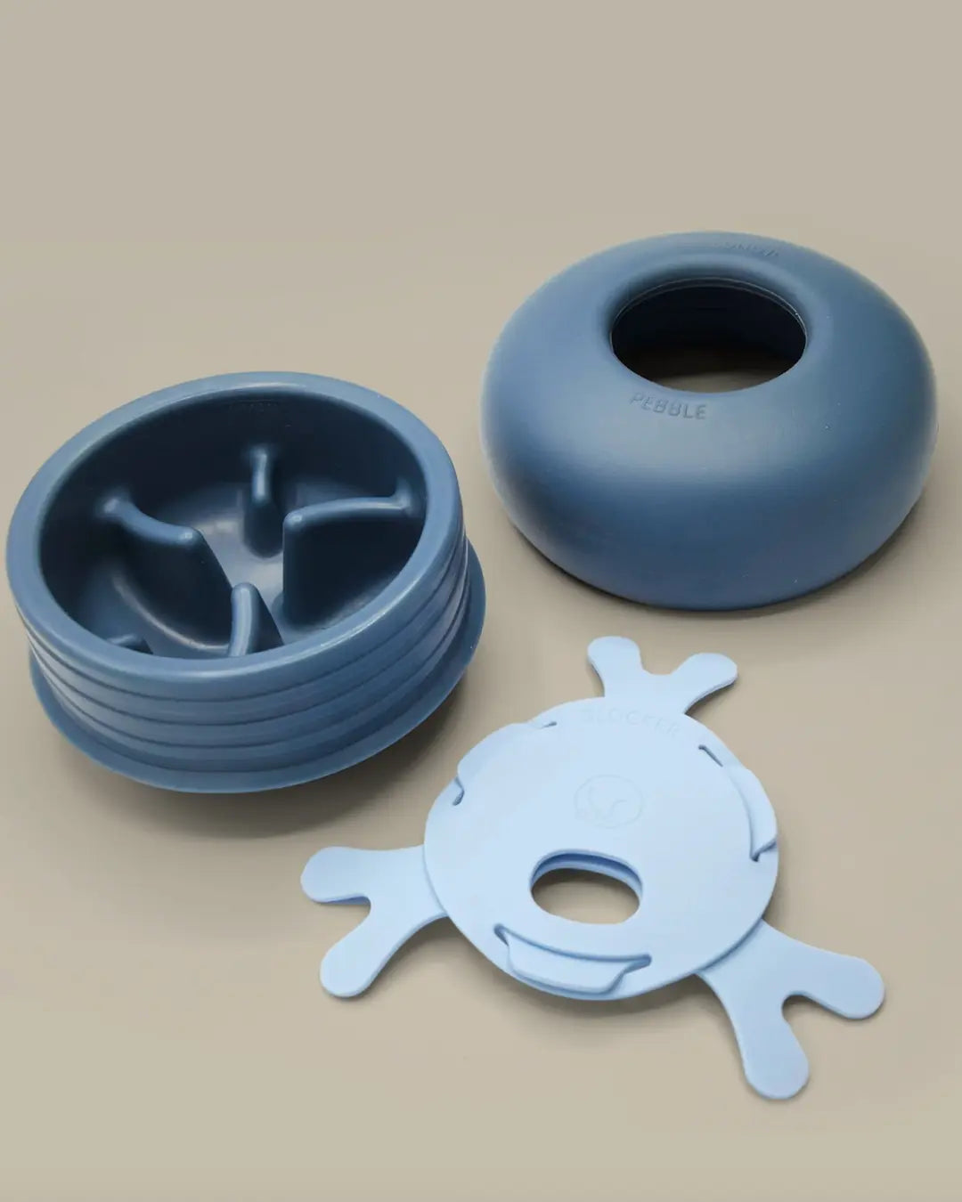 Deconstructed blue Lunoji pebble slow feeder and treat dispense on a beige background