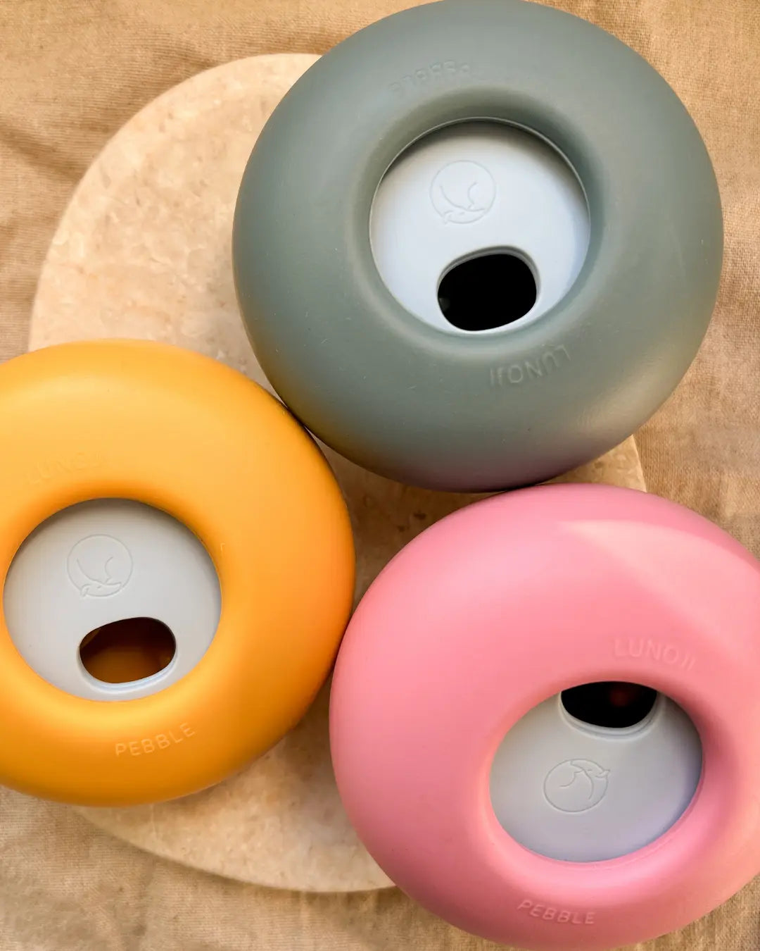 Three Lunoji dog slow feeders and treat dispensers in pink, blue and yellow on a neutral background