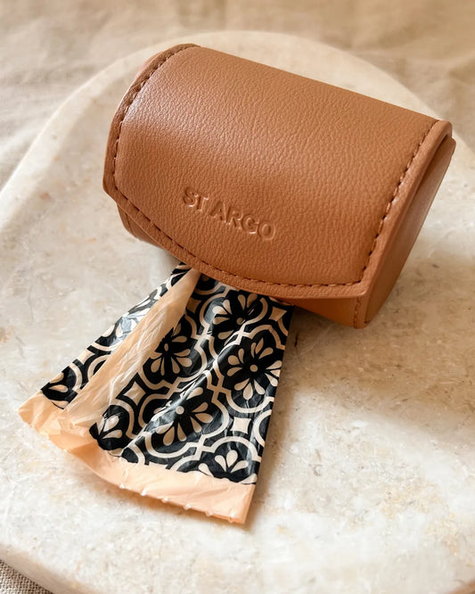 Brown luxury vegan leather poo bag case with a patterned poo bag inside on a beige surface