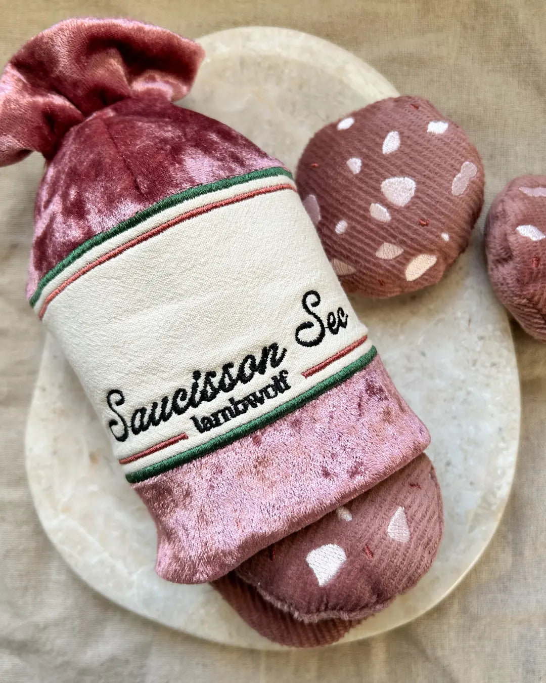 Saucisson sec-shaped dog toy with three plush squeaky salami toys on a neutral background