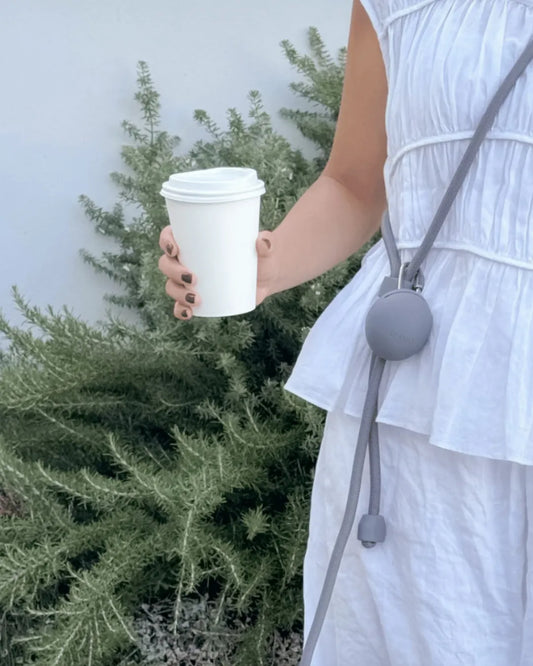 Lady holding a coffee cup with green bush and white outfit in background