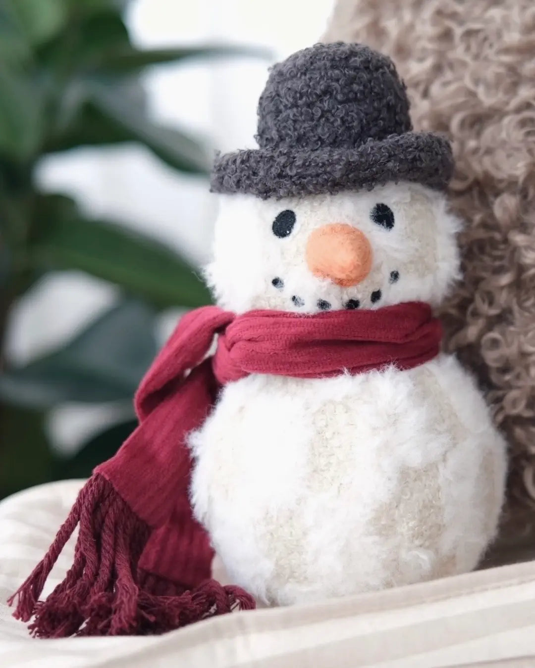 Plush snowman dog toy with a red scarf and grey hat on a white surface.