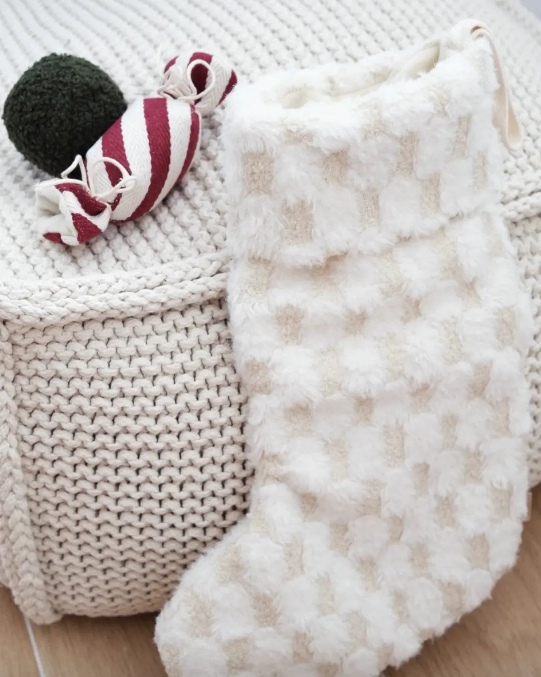 White textured dog toy-shaped Christmas stocking with a red and white striped toy on a textured surface