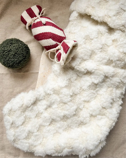 White fluffy dog toy stocking with a red and white striped toy on a beige surface