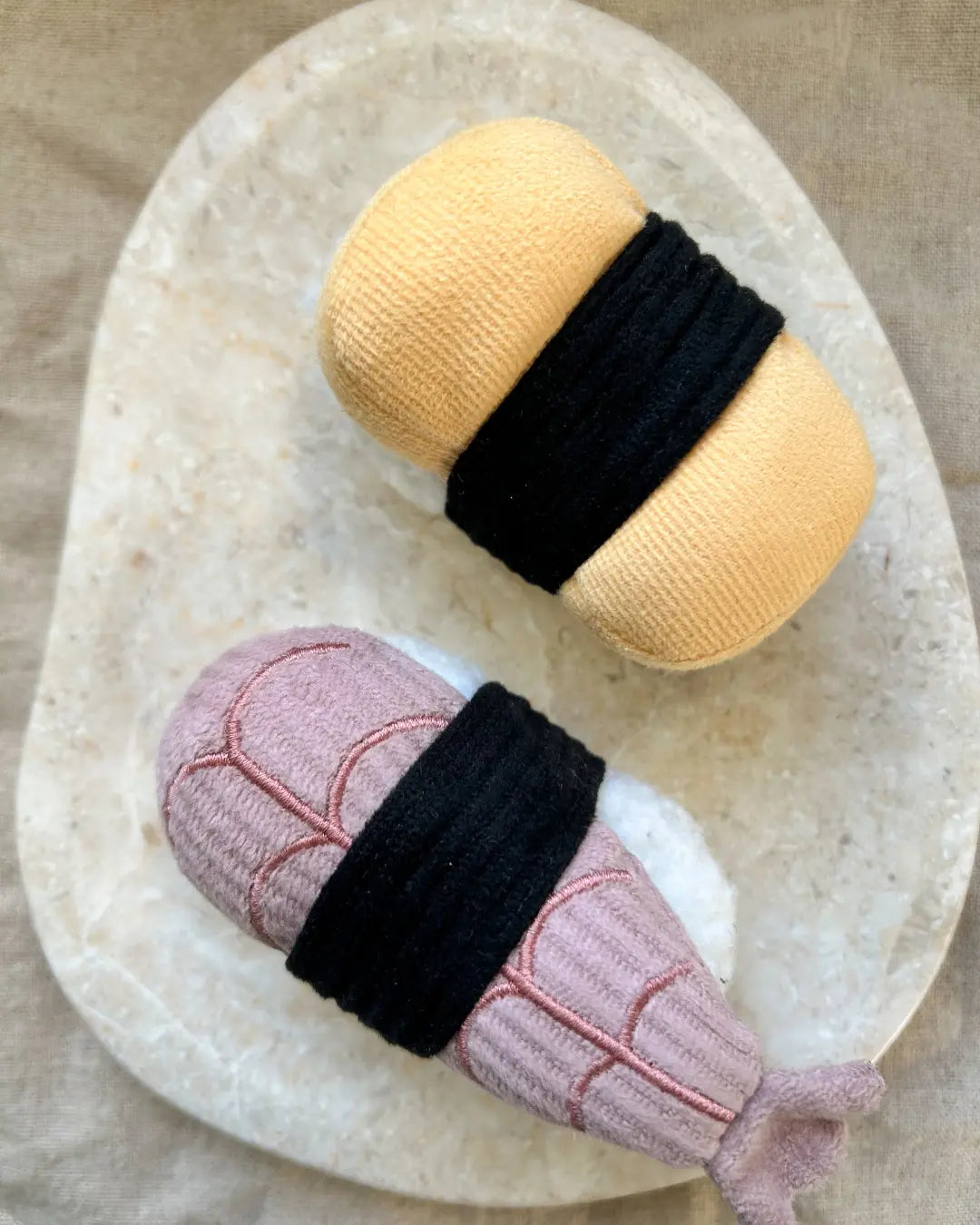 Two mini sushi-shaped plush dog toys on a beige marble background