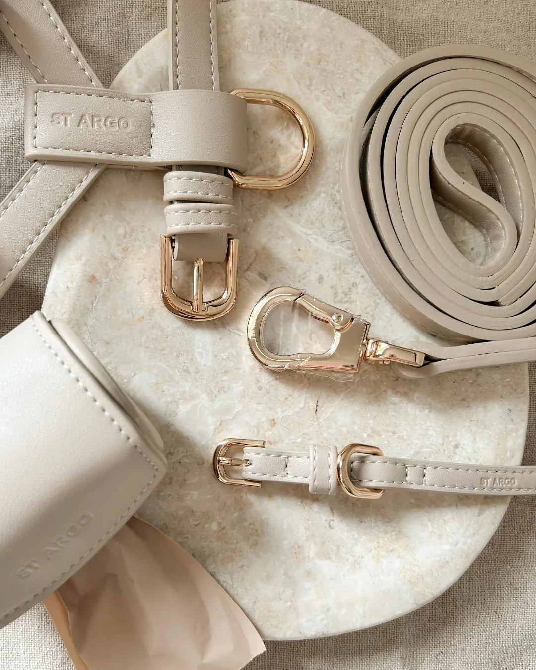 Beige luxury vegan leather dog harness, collar, lead and poo bag holder with gold hardware on a marble surface