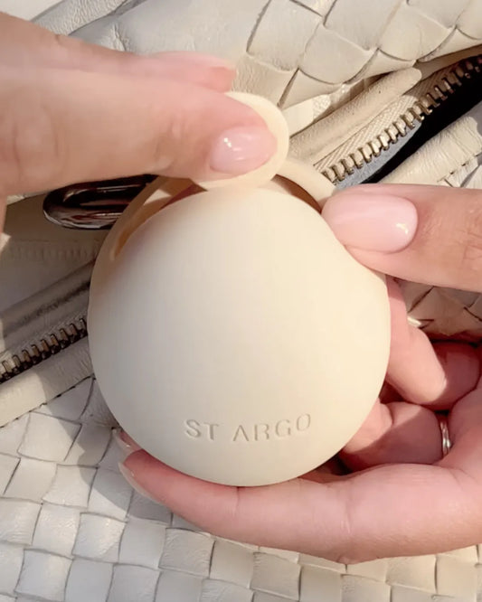 Person holding a beige egg-shaped dog treat pouch with 'St. Argo' branding against a textured surface.