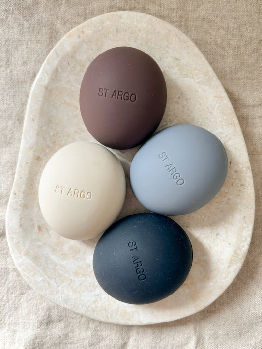 Neutral silicone luxury dog treat pouches in grey, black, cream, brown on a beige marble background