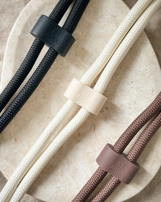 Three rope dog leads in black, cream and brown on a textured surface.