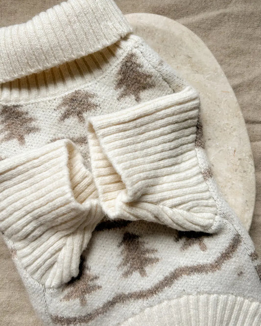 Close-up of a cream-colored knitted dog jumper with a Christmas tree pattern on a beige surface