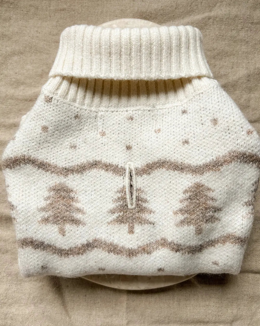 Knitted dog jumper with a Christmas tree pattern on a beige surface